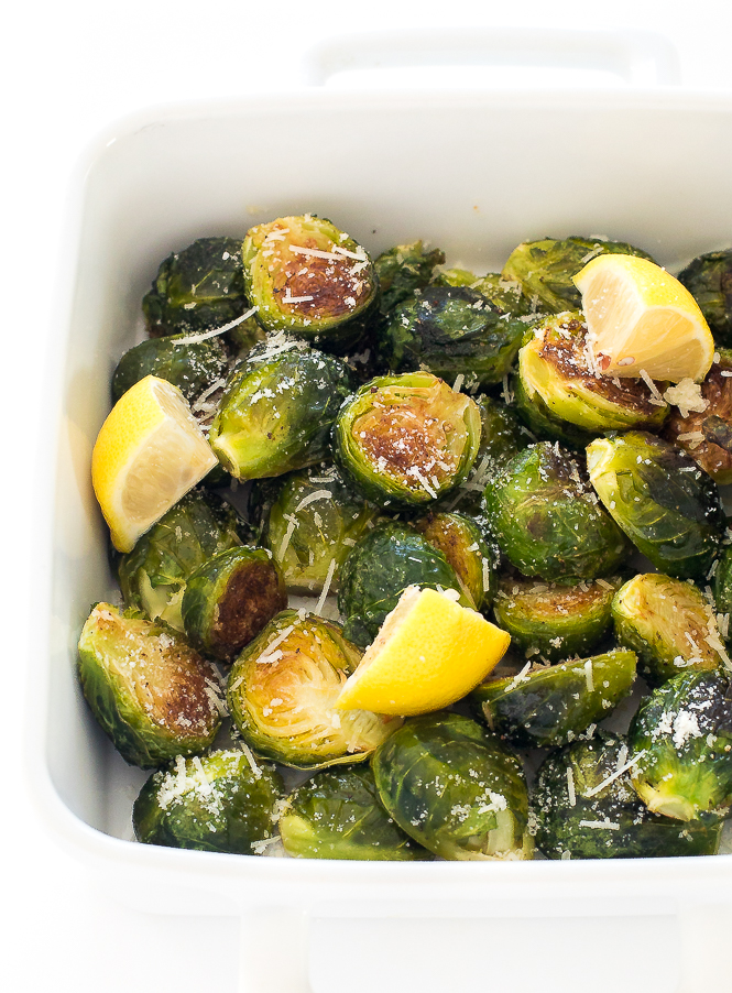 30 Minute Roasted Garlic Brussels Sprouts | chefsavvy.com Brussels sprouts in a white baking dish with lemon wedges on top.