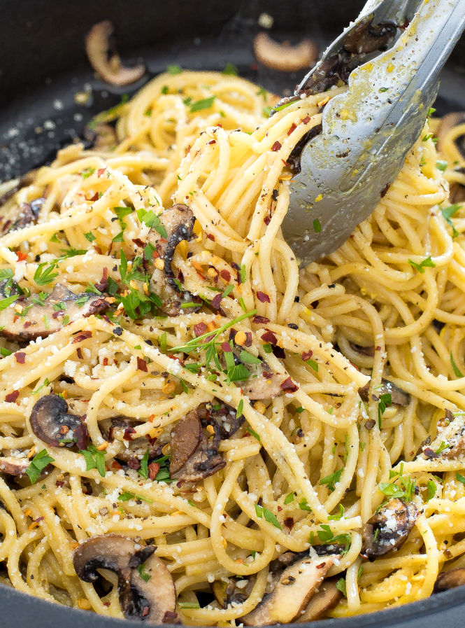 Metal tongs holding mushroom carbonara in a black skillet.