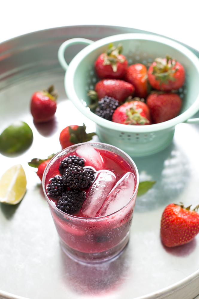 close up of Mixed Berry Mojito garnished with mint, berries scattered on table, colander in background