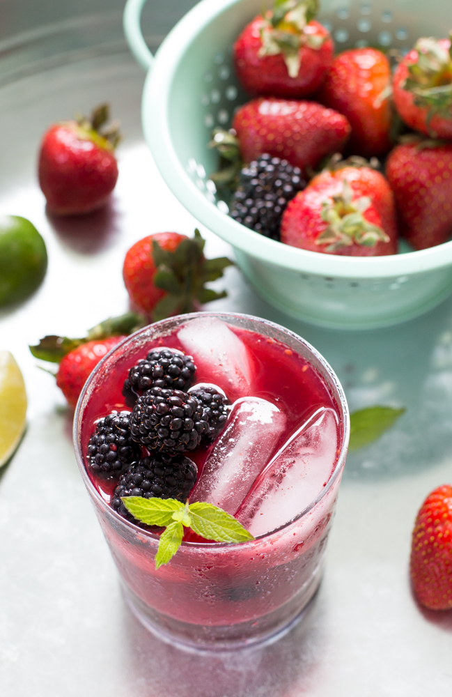 close up of Mixed Berry Mojito garnished with mint, berries scattered on table