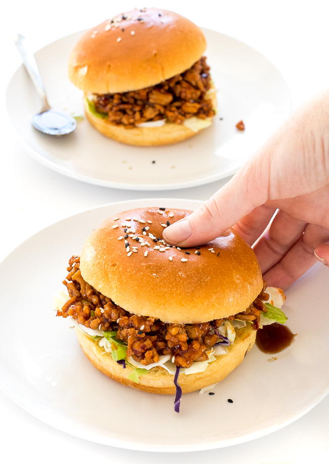 Easy Asian Sloppy Joes | chefsavvy.com Hand holding Asian Sloppy Joes on a white plate with another in the background.
