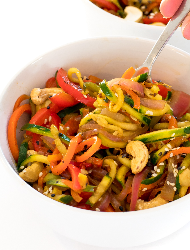 a white bowl filled with this zoodle stir fry and the author scooping up a bite with a fork 
