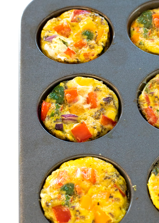 an side view of these easy egg muffin cups in a muffin tin with chopped peppers, onions, and spinach