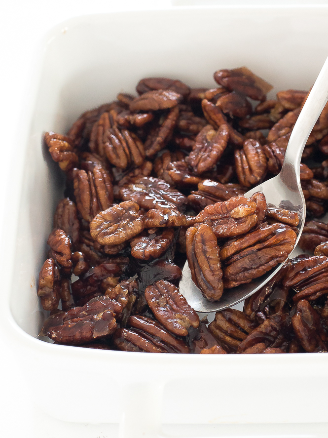 Candied Maple Pecans | chefsavvy.com Spoon lifting Maple Candied Pecans from a white dish.
