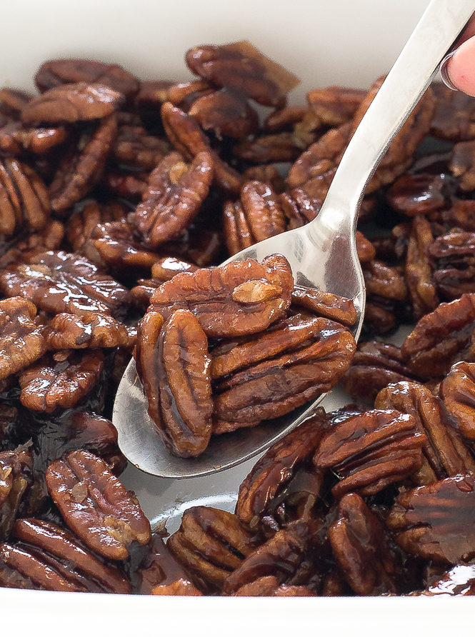 Maple Candied Pecans | chefsavvy.com Spoon lifting Maple Candied Pecans from a white dish.