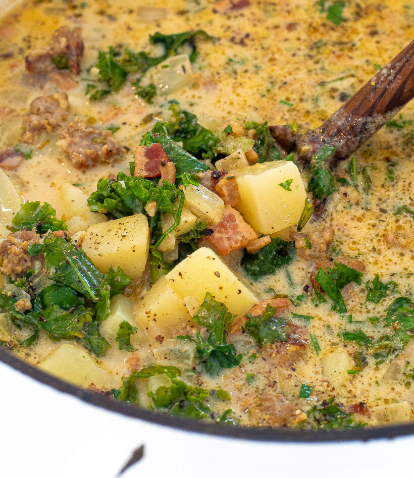 Soup in a dutch oven pot with a spoon scooping up a portion. 