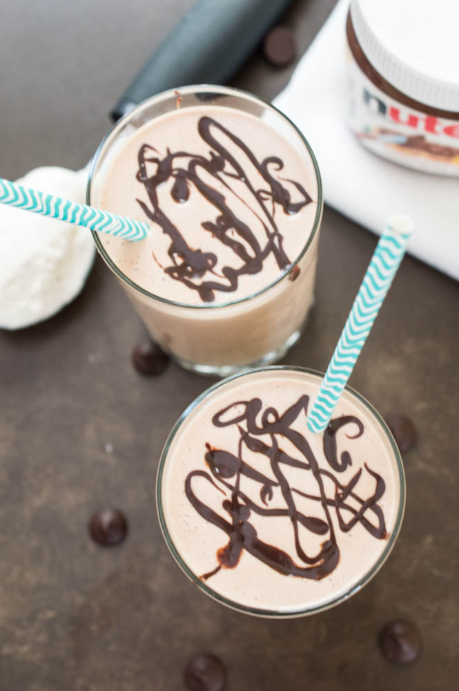 Easy Peanut Butter and Nutella Milkshake | chefsavvy.com overhead shot, 2 Peanut Butter and Nutella Milkshakes with chocolate swirled on top and blue chevron paper straws. Jar of nutella in background.