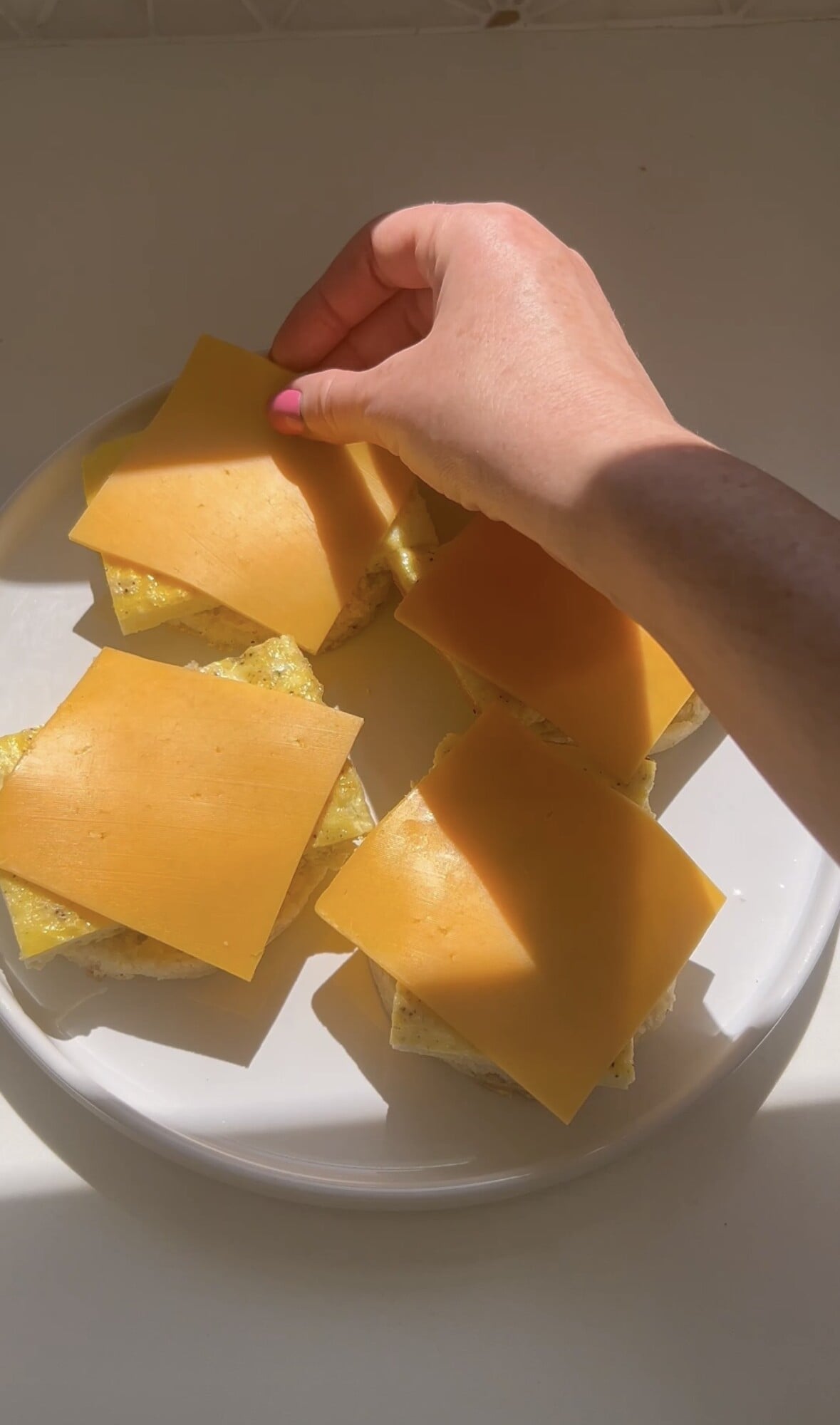 topping English muffins and egg with slices of yellow American cheese
