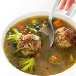a serving of this Turkey Meatball Vegetable Soup in a white bowl with a spoon