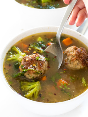a serving of this Turkey Meatball Vegetable Soup in a white bowl with a spoon