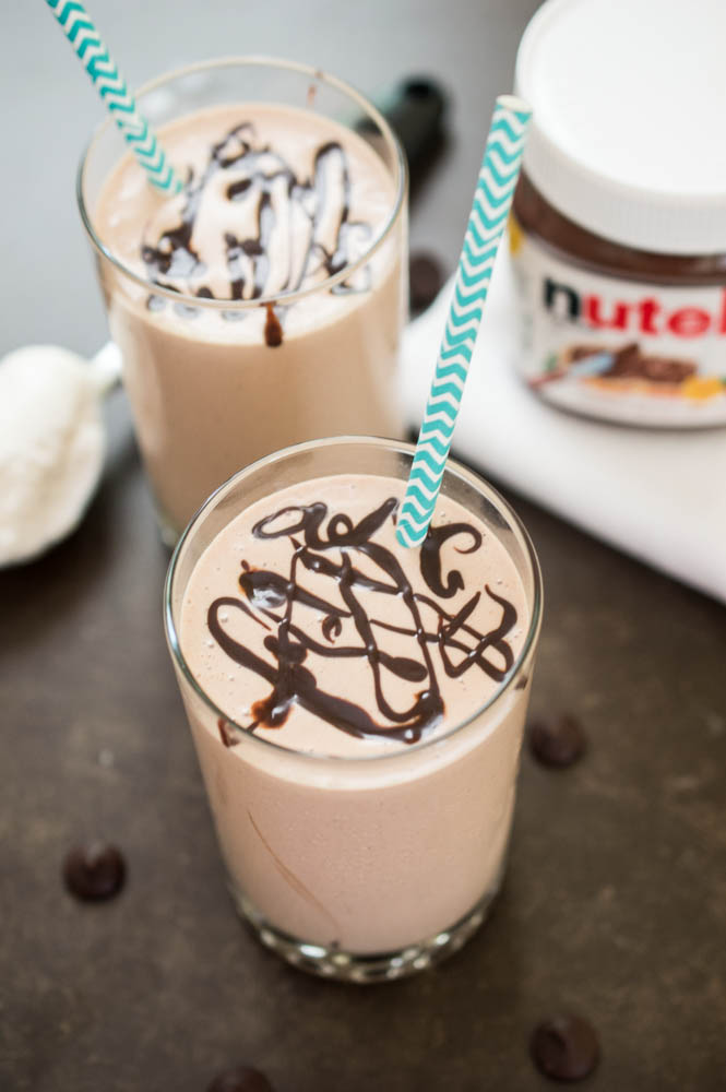 Nutella Milkshake | chefsavvy.com 2 Peanut Butter Milkshakes with chocolate swirled on top and blue chevron paper straws. Jar of nutella in background.