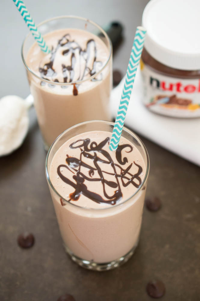 Easy Peanut Butter and Chocolate Milkshake | chefsavvy.com 2 Milkshakes with chocolate swirled on top and blue chevron paper straws. Jar of nutella in background.