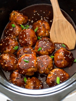 slow cooker sriracha meatballs inside a crock pot with a wooden spoon