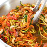 this zucchini noodle stir fry with cashews in a metal skillet with metal tongs tossing the noodles in the sauce | chefsavvy.com
