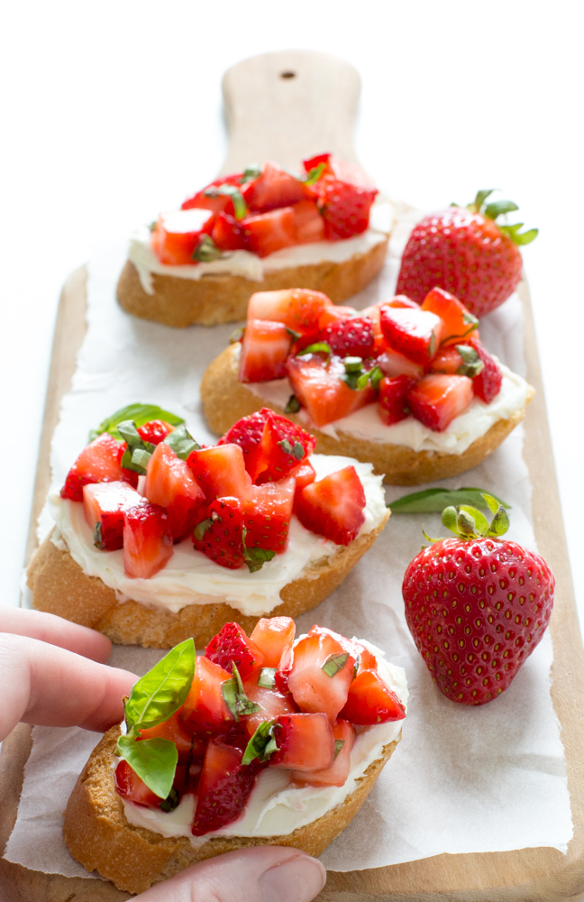 Strawberry Basil Bruschetta hand taking a slice of bruschetta off of a wooden board
