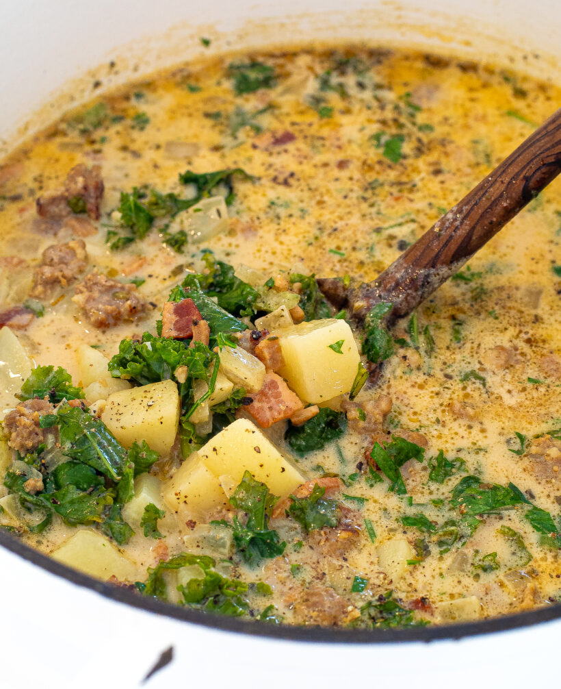 Close up shot of zuppa toscana in a dutch oven with a wooden spoon. 
