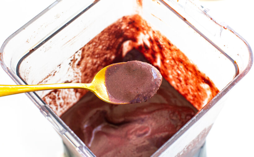 Acai smoothie bowl base in the blender after being blended with a spoon showing some of it to the camera. 