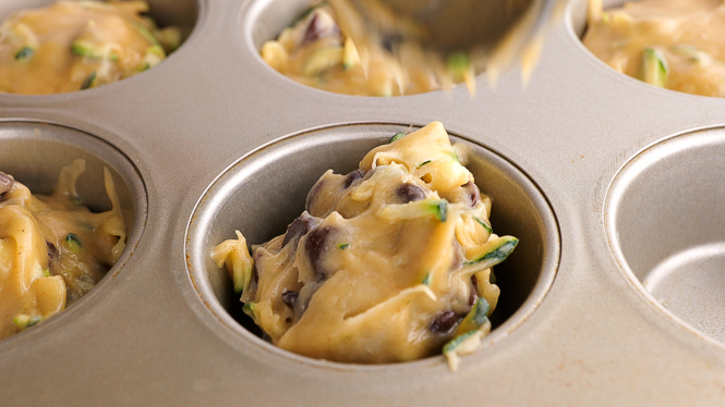 adding chocolate chip muffin batter to muffin tin