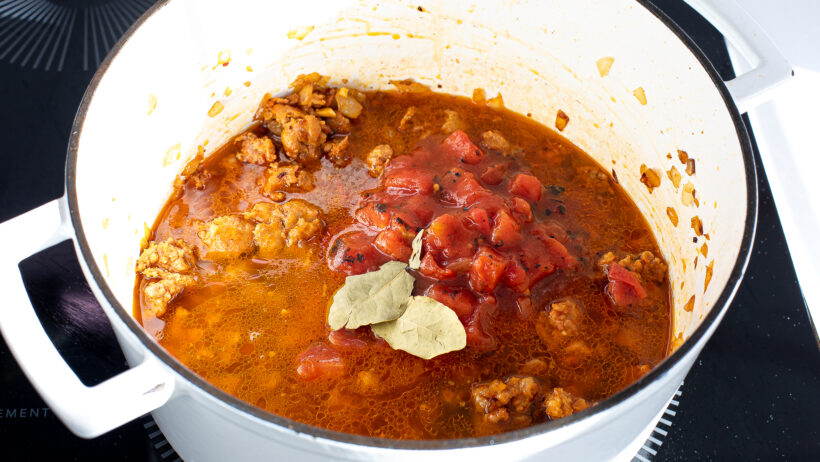 adding bay leaves and fire roasted tomatoes to cast iron pot