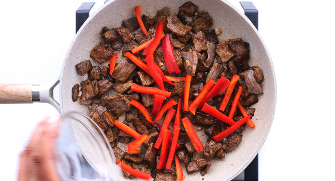 adding sliced red bell peppers to sliced beef in skillet