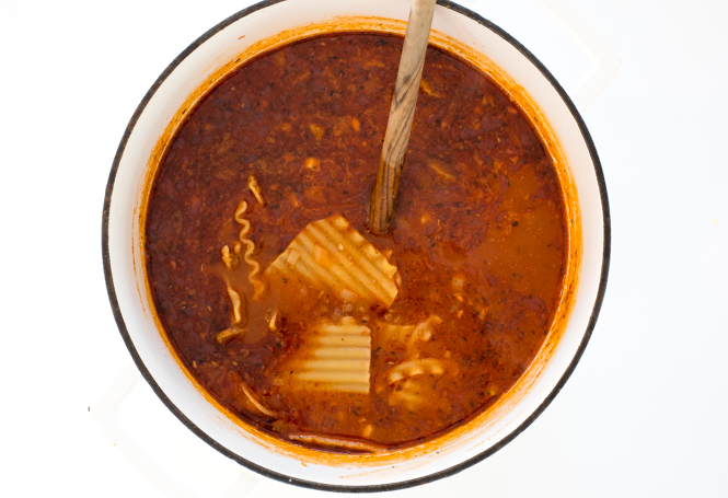 top shot of red soup in white bowl with noodles added