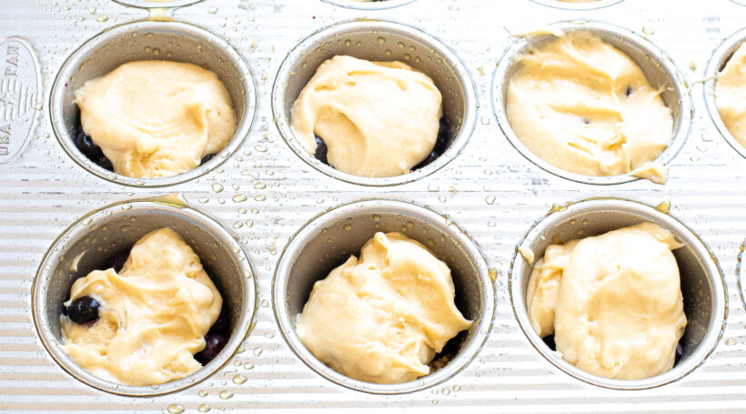Cake batter added on top of the blueberry layer in a muffin tin. 