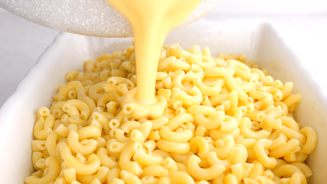 adding cheese sauce to elbow macaroni in a casserole dish