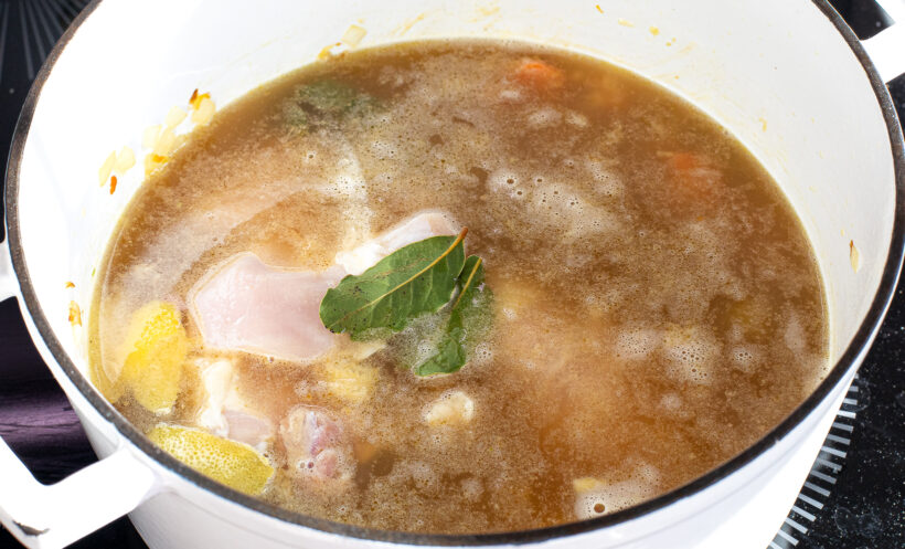 Chicken broth, raw chicken, bay leaves and lemon peel added to the soup pot. 