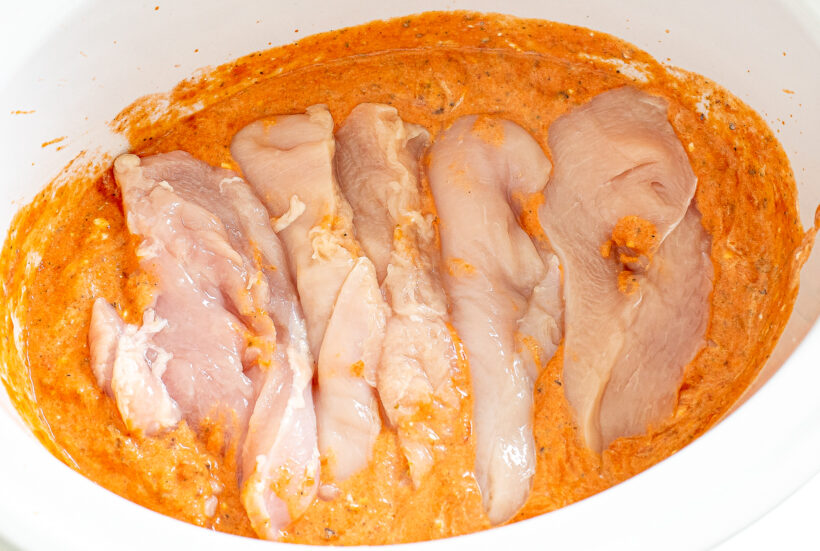 Raw chicken placed in the tomato sauce in the slow cooker.