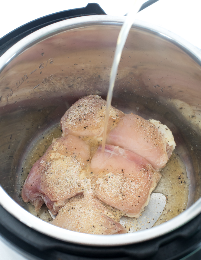 pouring chicken broth on top of frozen chicken thighs