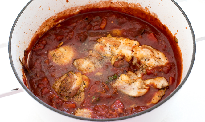 Chicken added to the red sauce in the white pot.