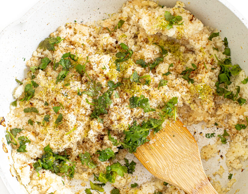 Cilantro and lime juice and zest being mixed into the cauliflower rice in a skillet.