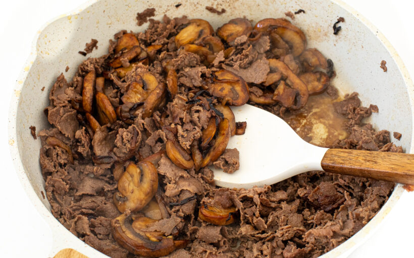 Sliced beef in a frying pan with onions and mushrooms added.