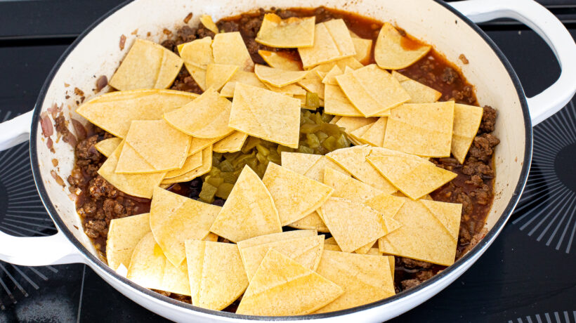 Corn tortillas added to meat mixture on the stove. 