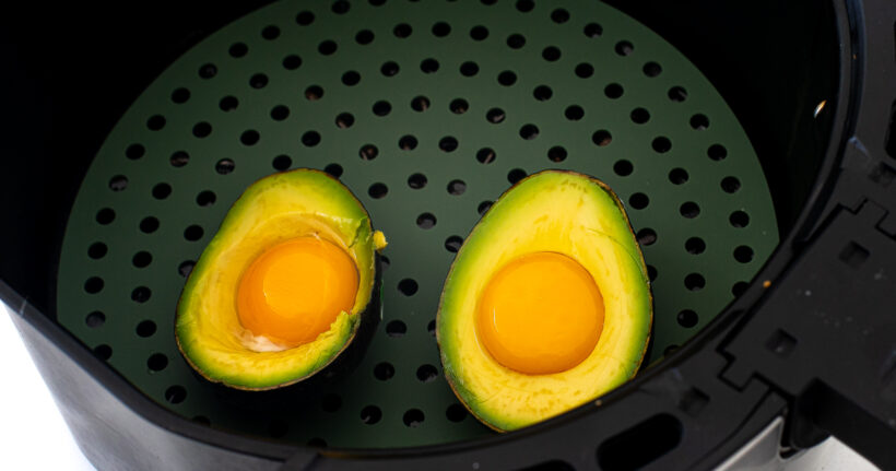 Two avocado halved with eggs in them in the air fryer.
