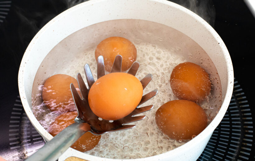 Using a ladle to gently lower eggs into a pot of boiling water.
