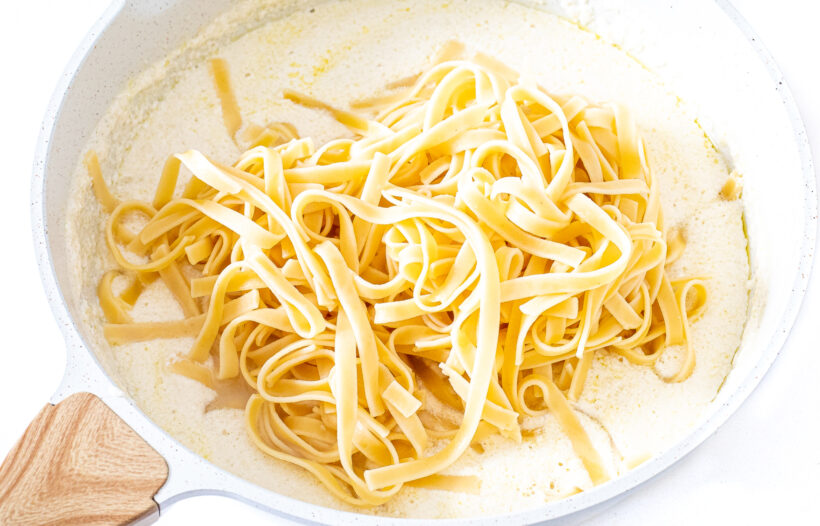Fettuccine noodles added to a skillet with alfredo sauce.