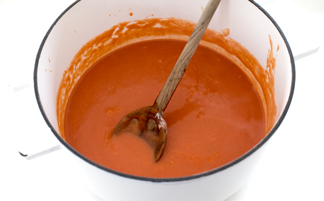 Tomato soup in white cast iron pot with wooden spoon