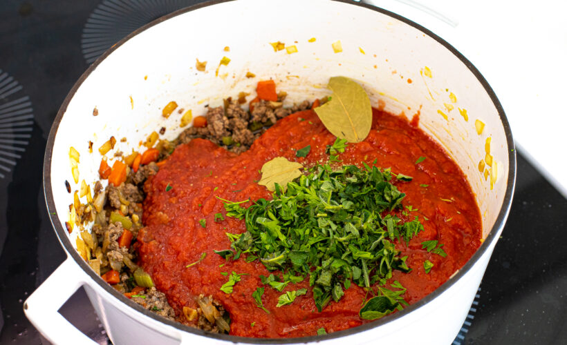 Tomato sauce and herbs added to meat and veggies in the pot.