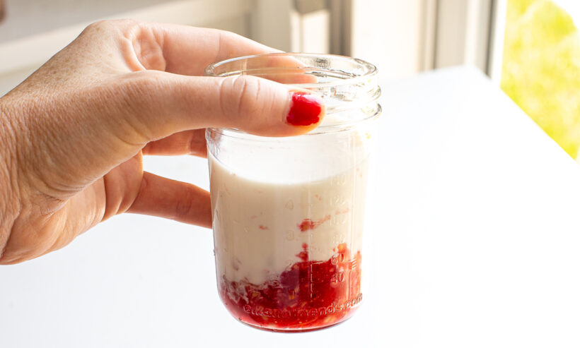 Hand holding a jar with muddled raspberries and Greek yogurt in it.