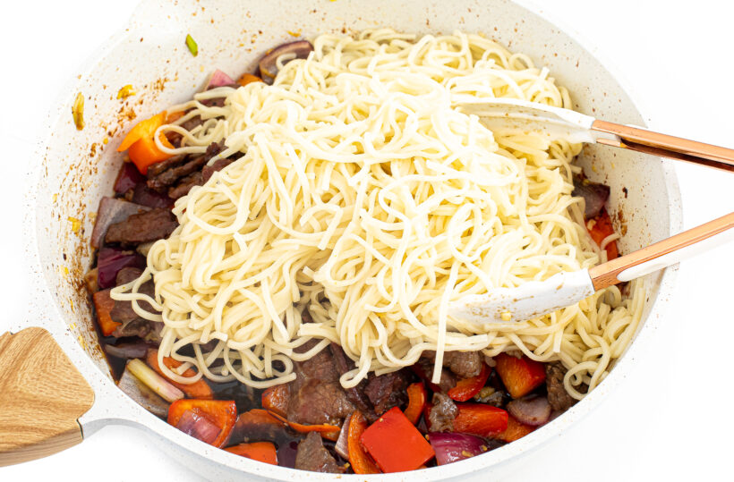 Rice noodles added to the skillet with steak and vegetables.