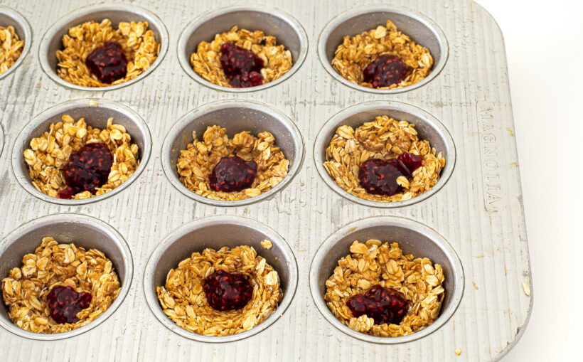 Oat cups in a muffin tip topped with dollops of raspberry jam.