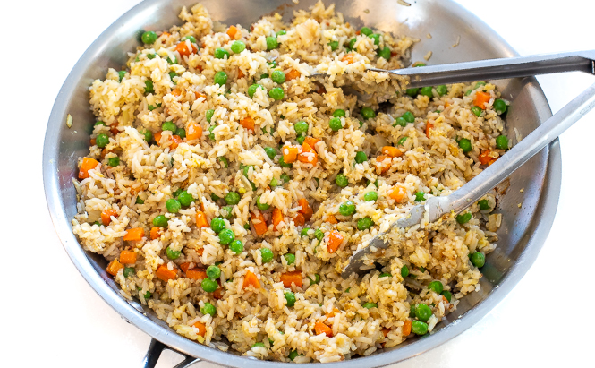 Cooking rice in a silver skillet with silver tongs. 