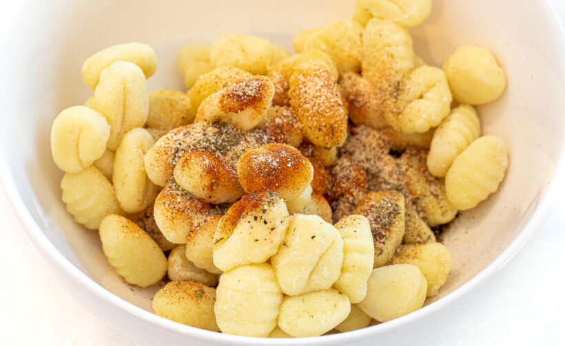Gnocchi in a small bowl with olive oil and spices in the bowl.