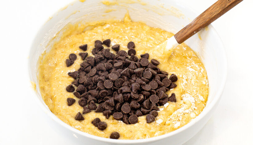 Muffin batter in a white bowl with chocolate chips and a rubber spatula.