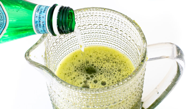 Pouring sparkling water into the pitcher of cucumber mint lemonade.