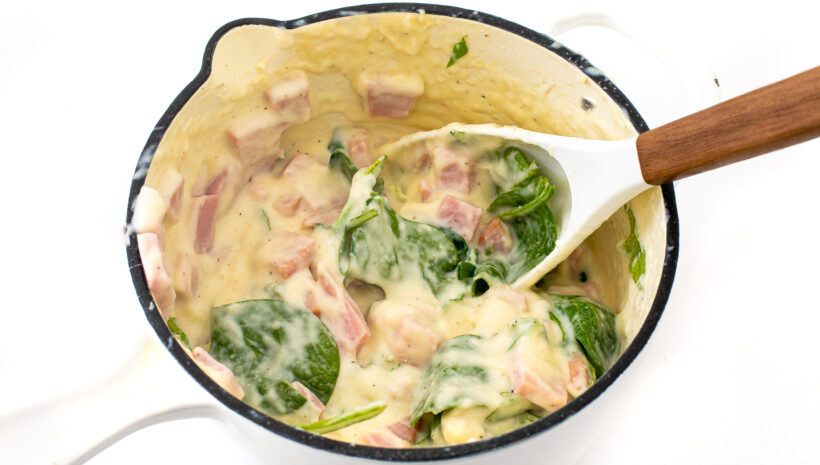 Ham and spinach stirred into the cheese sauce in a saucepan. 