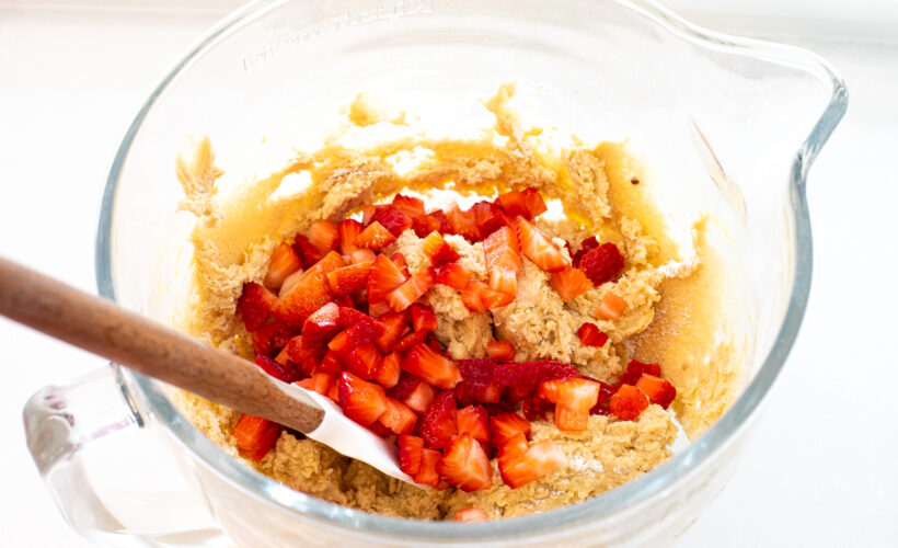 Strawberries being folded into the cookie dough with a rubber spatula.