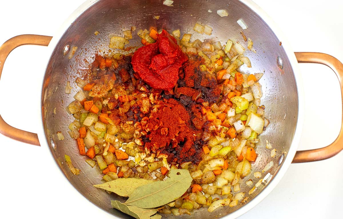 adding tomato paste and bay leaves to pot