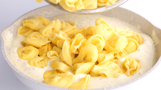 tossing tortellinis in Alfredo sauce